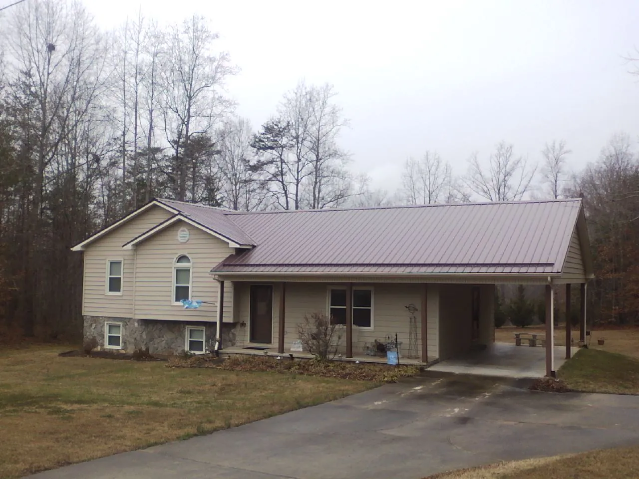 Burgundy metal roof on a tan split level home with an attached carport in Deep River