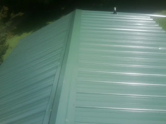 New green metal panels meeting at the ridge of a roof — Flat Roof Repair work by our crew in Deep River