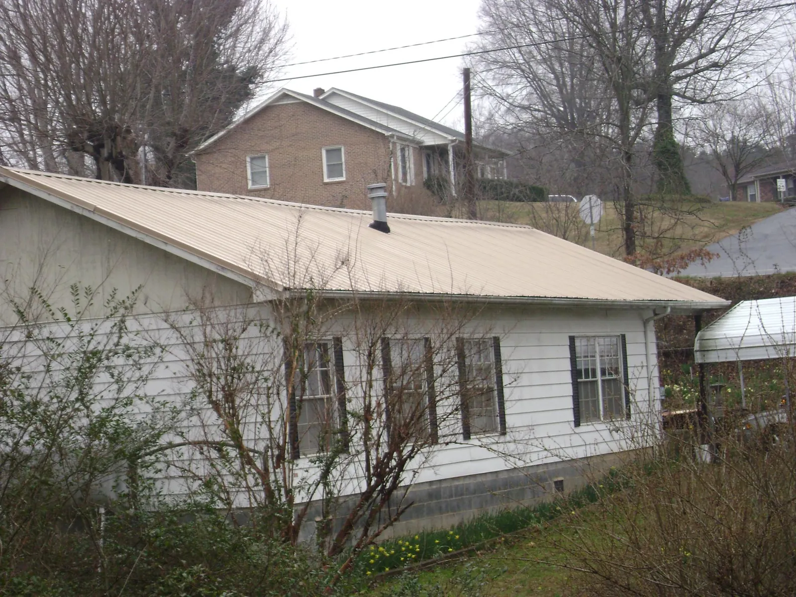 Tan metal roof on a white sided house set into a hillside — Commercial Roofing by Roofing Brothers in Deep River