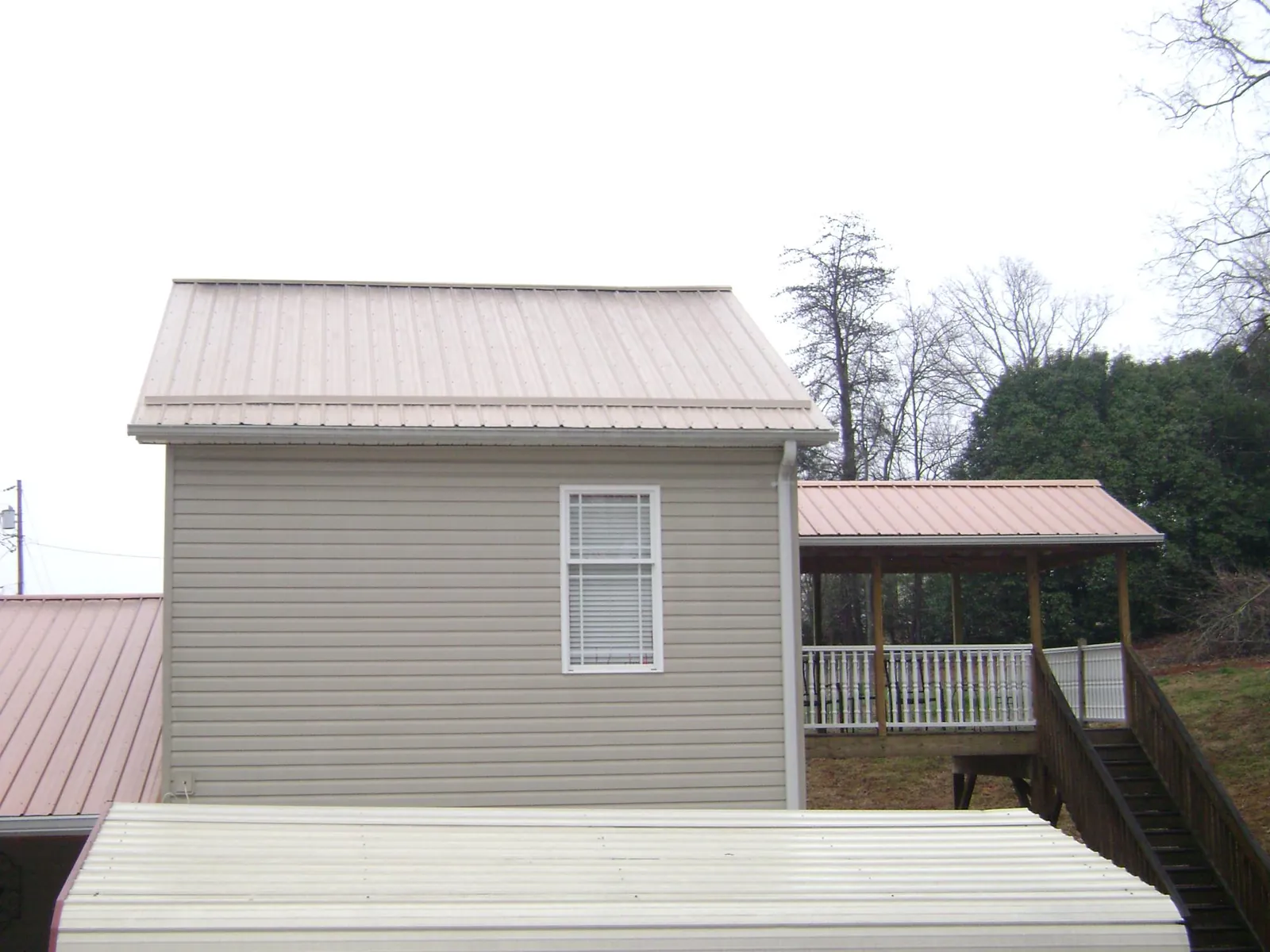 Tan metal roofs on a two story addition and attached porch, from a Roof Replacement job in Deep River